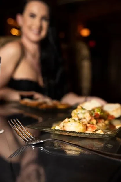 Seafood dish with vegetables and bread, blurred woman smiles in background.