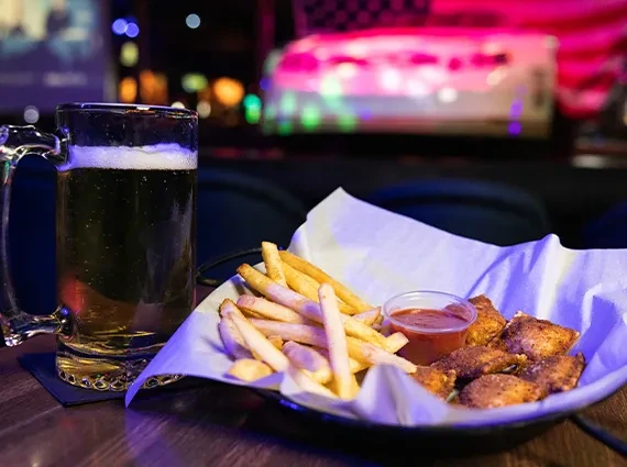 Mug of beer, fries, and chicken wings on a table, colorful bokeh.
