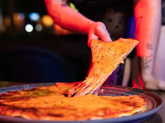 Hand pulls a cheesy pizza slice, melted cheese stretching, moody lighting.