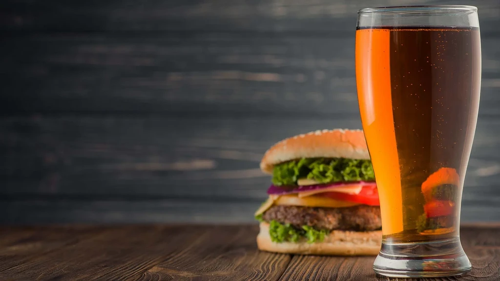 Close-up: bubbling amber drink, classic burger on a rustic table.