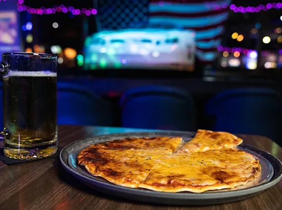 Cheesy pizza and lager beer on a dark pub table.
