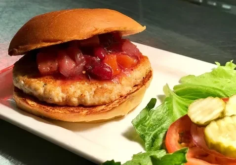 Close-up of a burger with fruit salsa, side salad, and pickles.