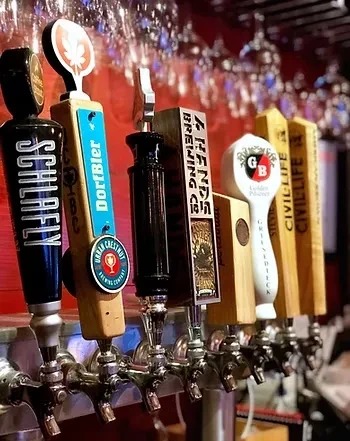 Seven distinct beer tap handles with brewery names at a bar.
