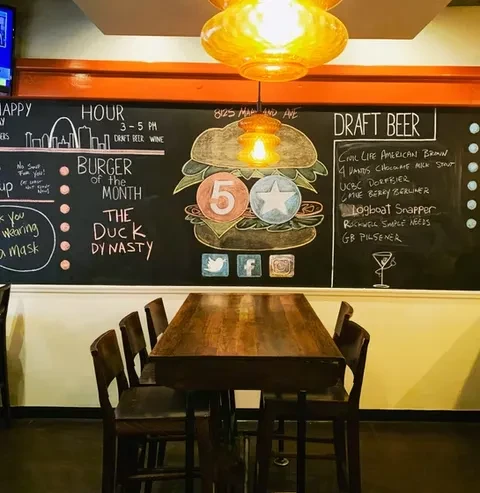Restaurant interior featuring a chalkboard menu, burger art, and communal table.
