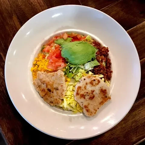 Colorful bowl with grilled meat, avocado, rice, lettuce, and crumbled meat.