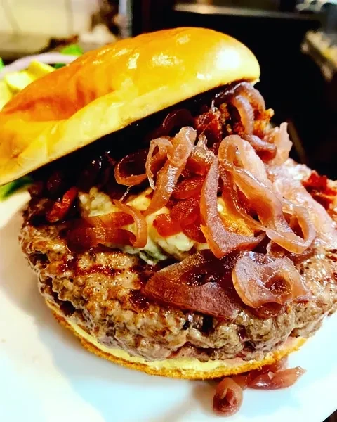 Close-up of a gourmet burger with brioche bun, beef, caramelized onions, sauce.