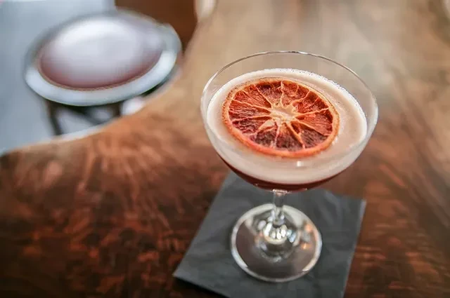 Reddish-brown cocktail in coupe glass, with frothy foam and dried citrus.