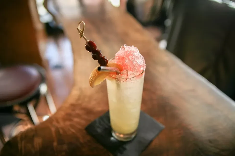 Tall cocktail with pink crushed ice, citrus wedge, and red berries.