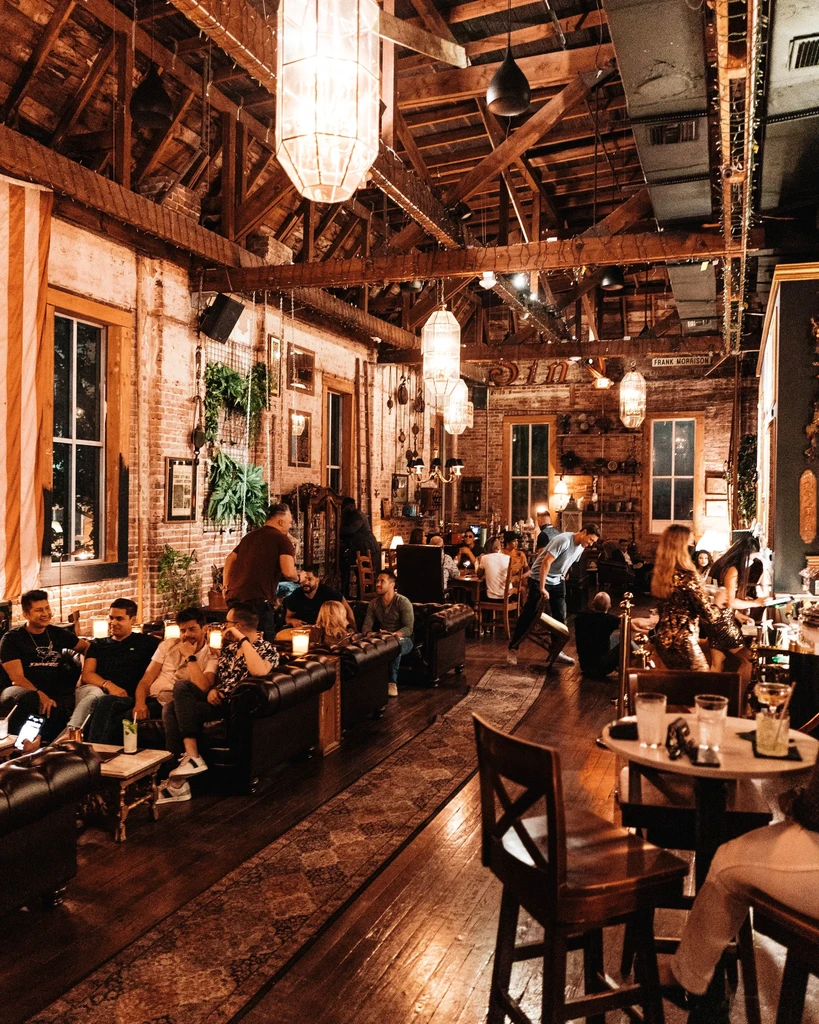 Warmly lit restaurant interior with exposed beams, brick walls, and people.