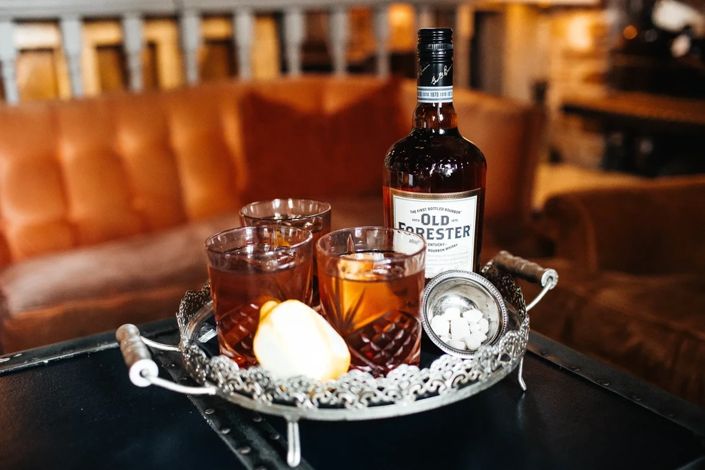 Old Forester bourbon bottle, three whiskey glasses, lemon, sugar on tray.