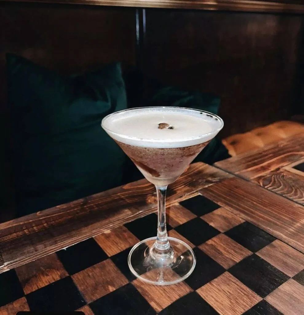 Layered martini cocktail with foam and coffee garnish on checkerboard table.