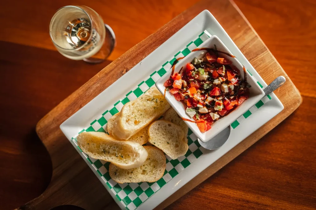 Overhead: Bruschetta with tomatoes, mozzarella, herbs, toasted bread, white wine.