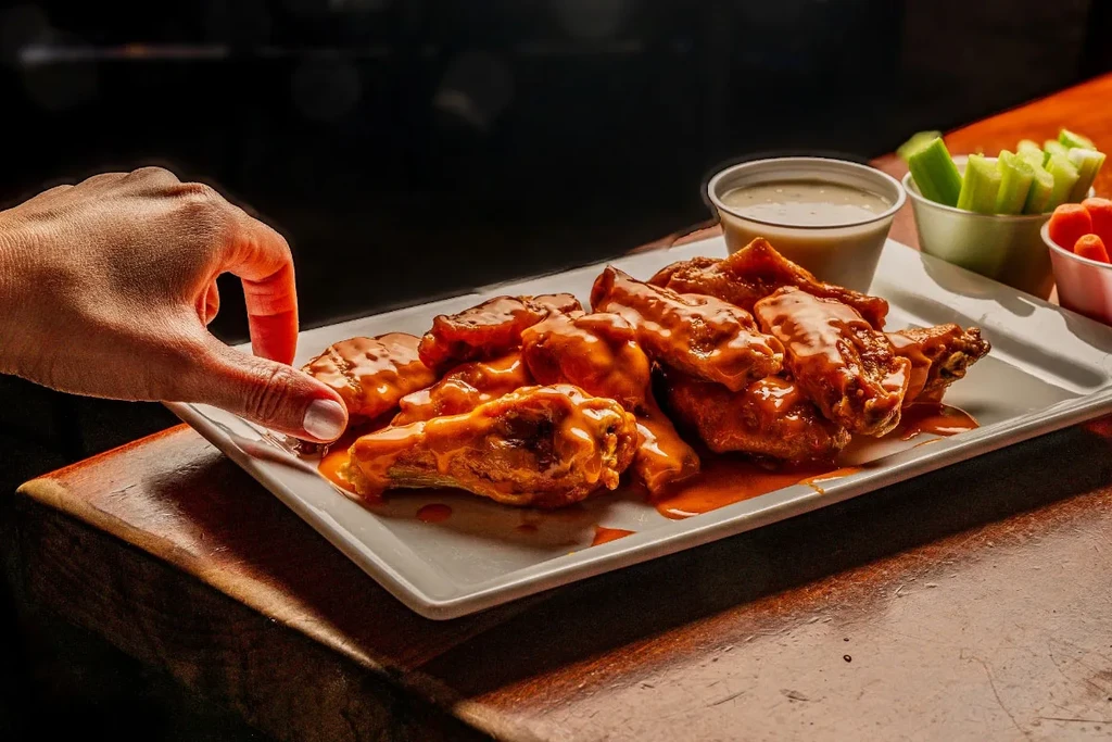 Close-up: Buffalo wings in orange sauce with creamy dip and vegetables.