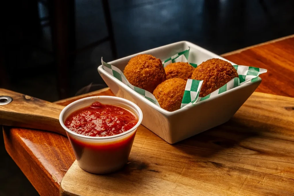 Golden-brown fried arancini with red sauce on a wooden board.