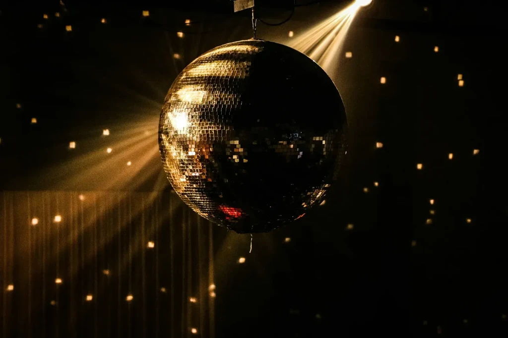Large mirrored disco ball casting light beams in a dark room.