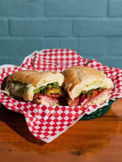 Generously filled submarine sandwich halves served in a green plastic basket.