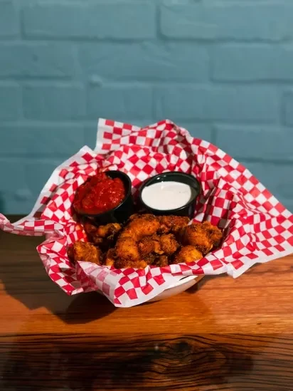 Crispy fried food in a bowl with red and white dipping sauces.