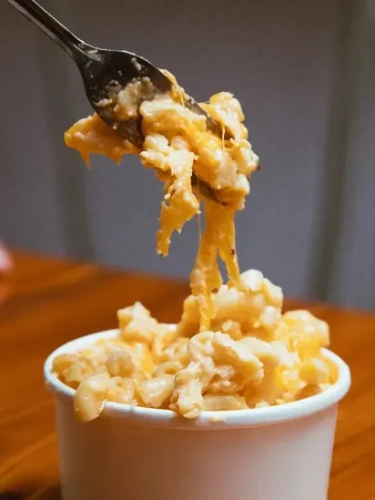 Fork lifts creamy, stretchy mac and cheese from a white cup.