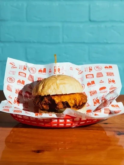 Crispy fried chicken sandwich with melted cheese, pickle, in a red basket.