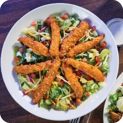 Large salad bowl with chicken tenders, mixed greens, cheese, and dressing.