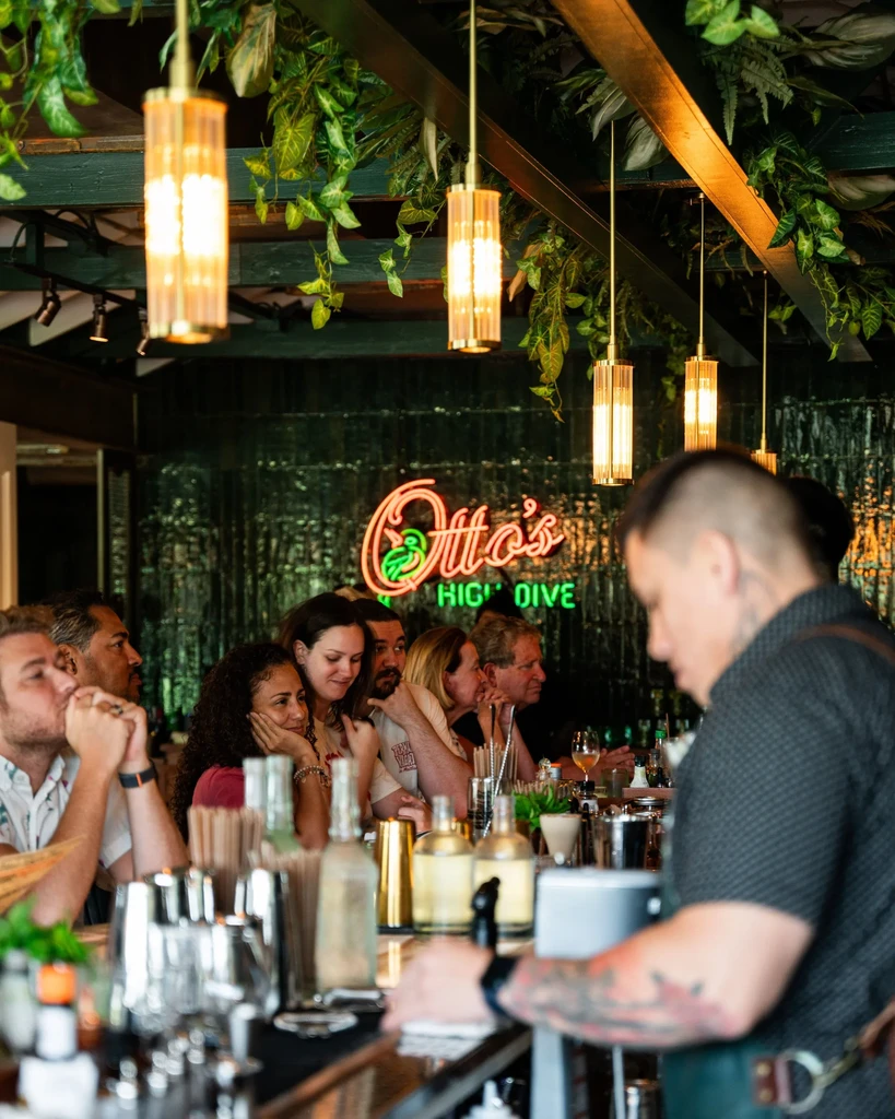 Warmly lit bar interior with customers, bartender, and Otto's HIGH DIVE sign.