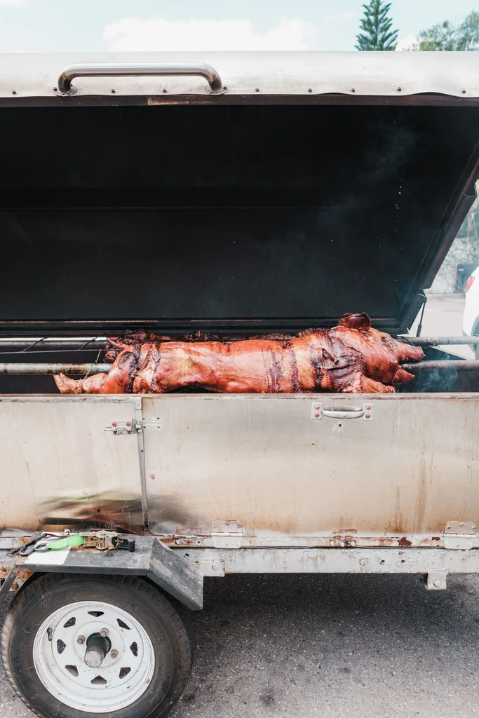 Reddish-brown whole roasted pig cooking in an outdoor trailer rotisserie.