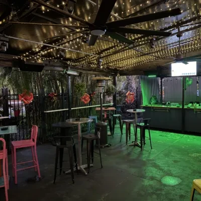 Outdoor patio at night with string lights, high tables, and green bar.