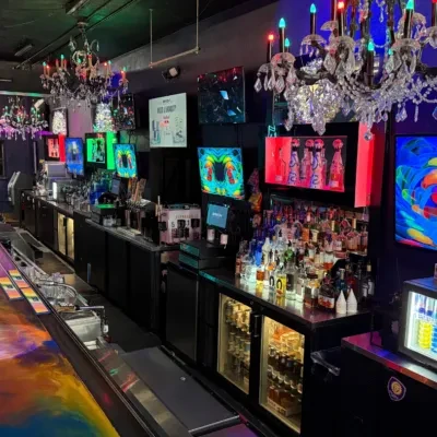 Vibrant, multi-colored bar counter, screens, and chandeliers in a dark lounge.