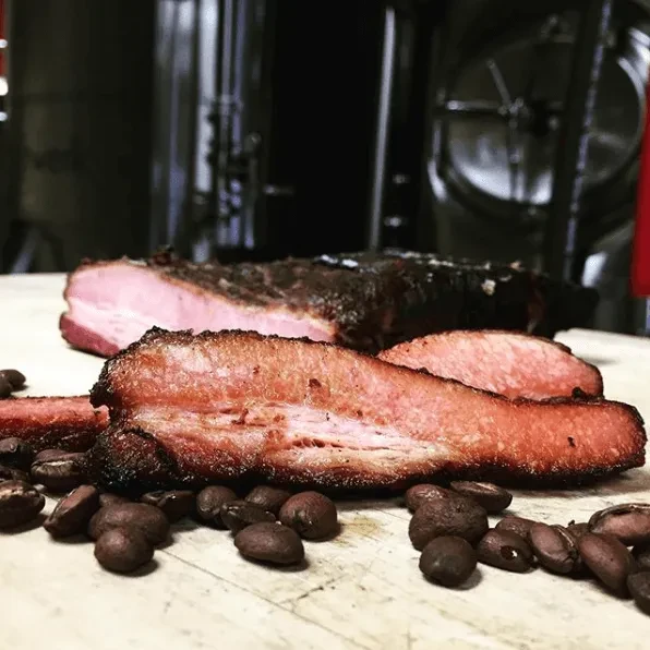 Smoked meat slices and beans on wood, blurred industrial background.