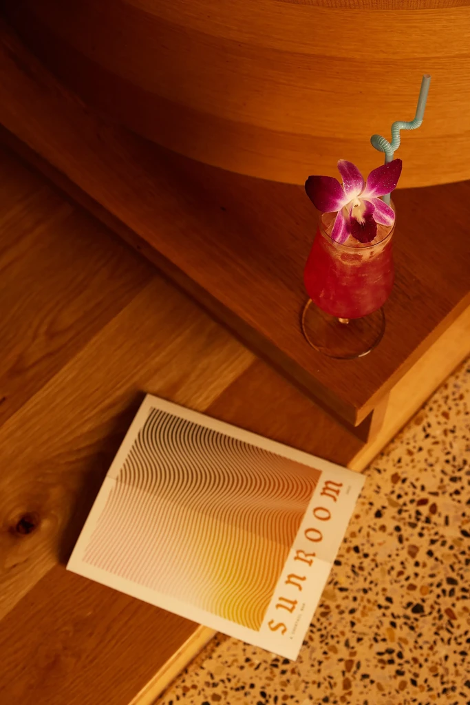 Red cocktail with purple orchid, light blue straw, 'SUNROOM' magazine.