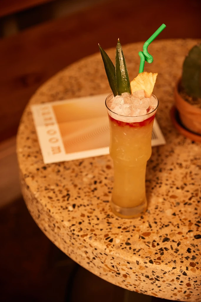 Cocktail in bamboo glass with pineapple and straw on terrazzo table.