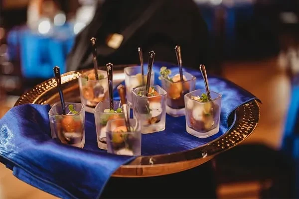 Golden tray, blue fabric, eight glasses of layered food with garnishes.