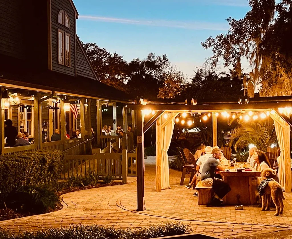 Restaurant exterior at dusk with outdoor dining, string lights, and a dog.