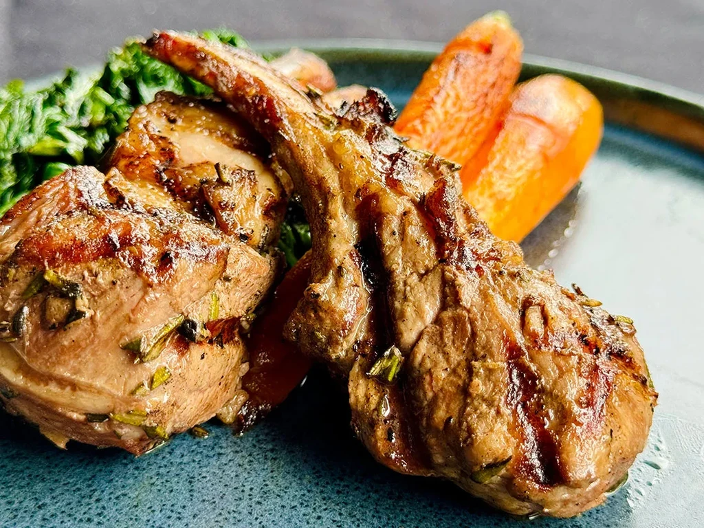 Grilled lamb chops with herbs, green vegetables, and carrots plated.