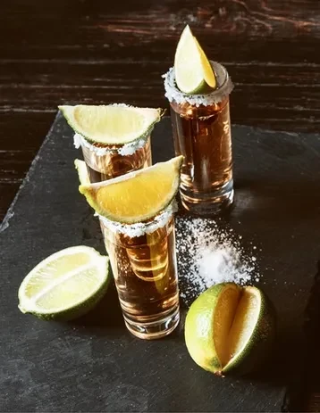 Three brown liquor shots, two with salt rims and lime wedges.