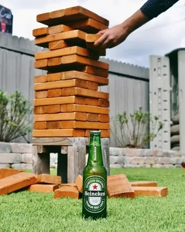 Heineken bottle on grass, hand extracting block from Jenga tower.