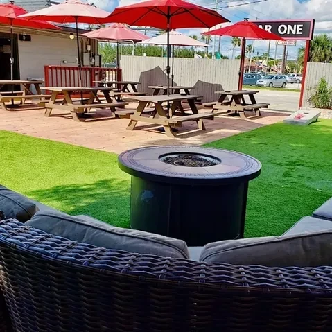 Bar One's sunny outdoor patio with picnic tables and red umbrellas.