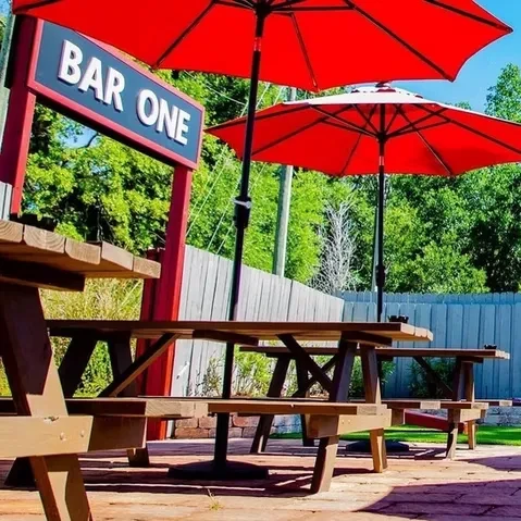 Sunny Bar One patio with empty wooden tables and red umbrellas.