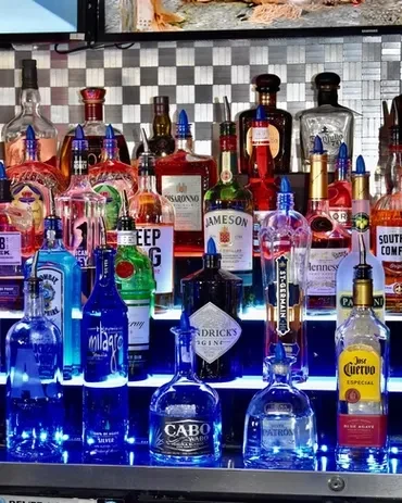 Variety of liquor bottles on bar shelves illuminated by blue LED lights.