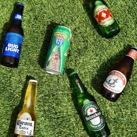 Assorted beer bottles and a can with condensation on green turf.