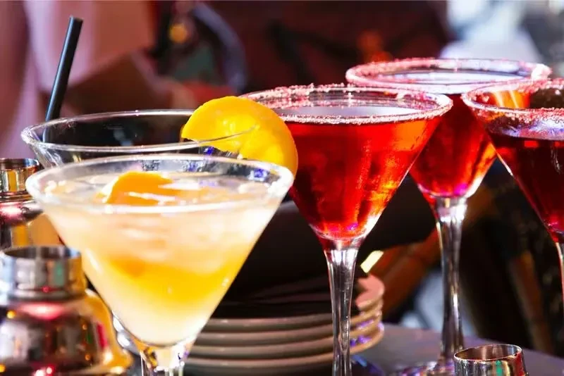 Five martini cocktails on a bar, three red, one yellow.