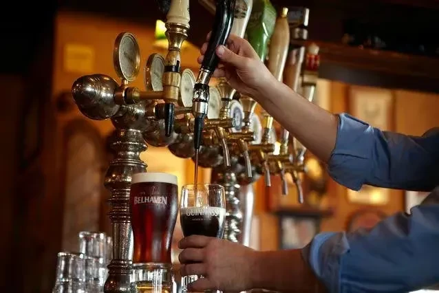 Bartender pours Guinness from tap, amber beer sits on bar.