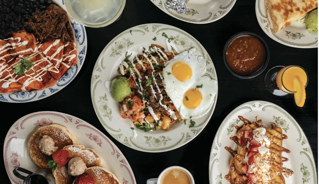 Overhead flat-lay: Diverse breakfast and brunch spread on dark table.