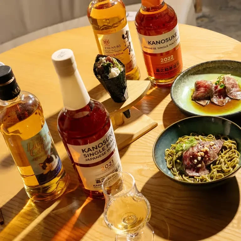 Overhead: Japanese whisky bottles, glass, sushi, seared meat, and noodles.