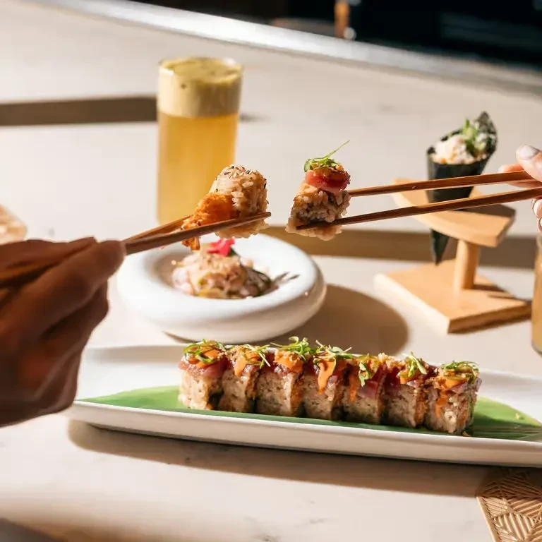 Close-up of sushi, temaki, and drinks on a counter, hands holding rolls.