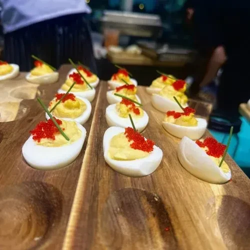 Deviled eggs with red caviar and chives on a wooden board.