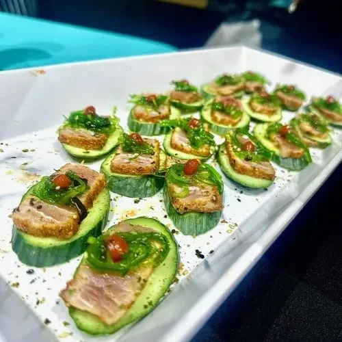 Cucumber canapés topped with seared fish, seaweed salad, and red garnish.