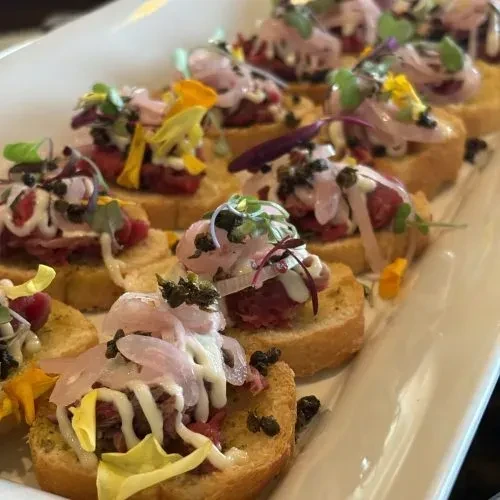 Close-up of gourmet canapés with tartare, creamy sauce, and fresh garnishes.