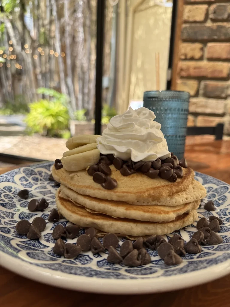 Stack of three pancakes with whipped cream, chocolate chips, and banana.