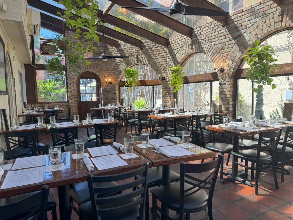Bright, rustic dining room with brick, arched windows, glass ceiling, set tables.